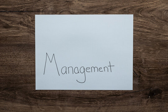 Flat lay background white sheet of paper with negative space and the word Management handwritten on lower portion on paper.