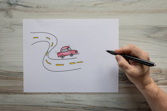 Photo of hand drawn graphic of red vehicle driving on a wavy road birds eye view with hand holding a black ink pen. Traveling road trip concept.