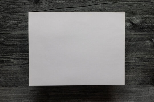 Birds eye view of blank sheet of paper against a dark grey wooden background.