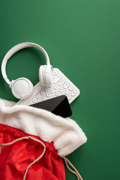 Holiday tech gifts in a Santa present bag with headphones and smartphone for Merry Christmas and Happy New Year on vertical green background