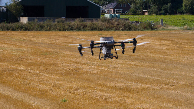 Aerial view of an agricultural drone spraying a harvested field with farm buildings in the background in Onstwedde, Groningen, Netherlands.