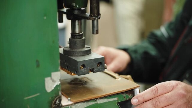 Hand operated press embosses a logo die onto a leather panel in a green machine