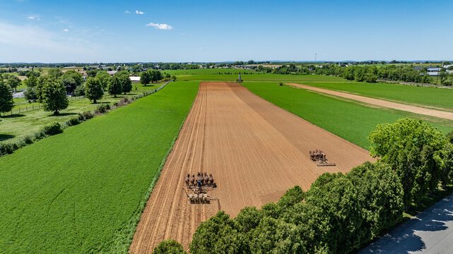 Aerial view of Amish farmers working the fields with teams of horses in the rural landscape of Gordonville, Pennsylvania, United States.