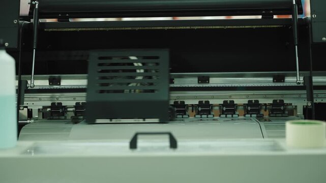 Wide format printer carriage runs along a metal rail above a roll of printed media