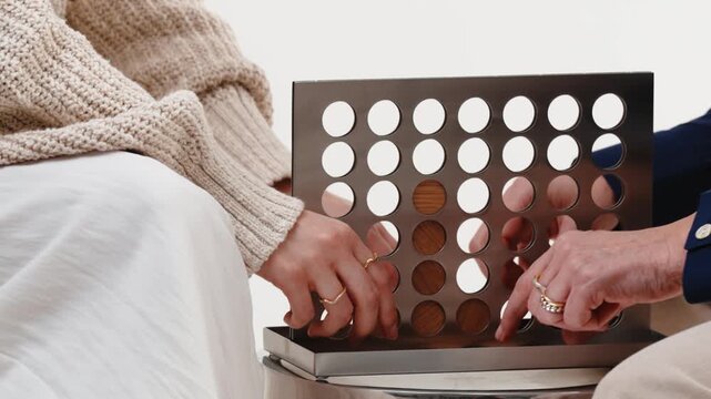 Connect Four grid with wooden discs dropped by two people playing at a bright table