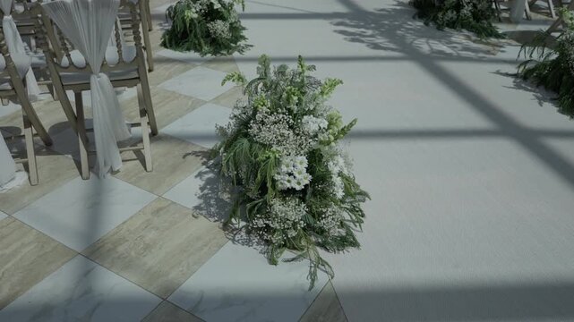 White flowers and greenery on a checkerboard marble floor beside draped chairs at a ceremony