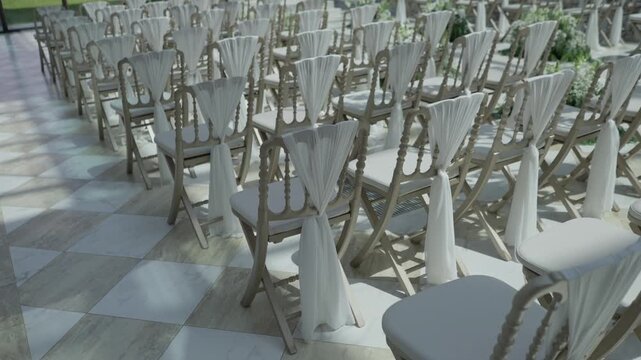 Empty chairs with white fabric drapes lined in rows on a checkerboard marble floor before a ceremony