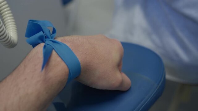 Blue tourniquet tied around a forearm as a healthcare worker holds cotton over the puncture site