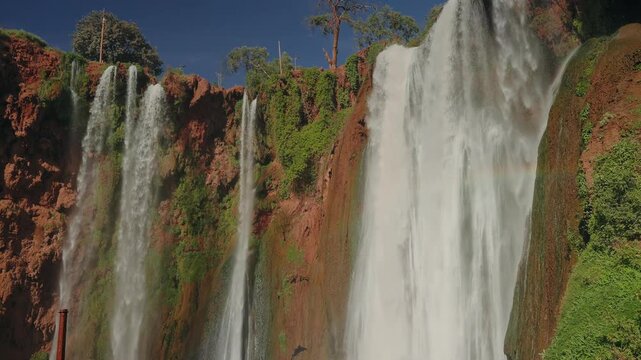 Ouzoud Falls plunging down red cliffs with green vegetation under blue sky Morocco