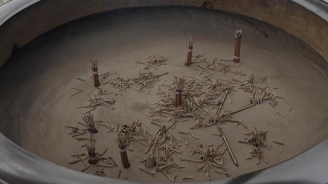 Bundles of burnt incense sticks standing in the ash of a large temple censer