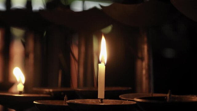 Single votive candle burning on a metal holder in a dark shrine interior in Japan