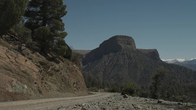 Gravel mountain road cutting past rock cliffs below a plateau in the Atlas Mountains Morocco