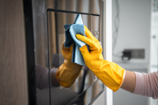Washes the oven glass in the kitchen with a glove