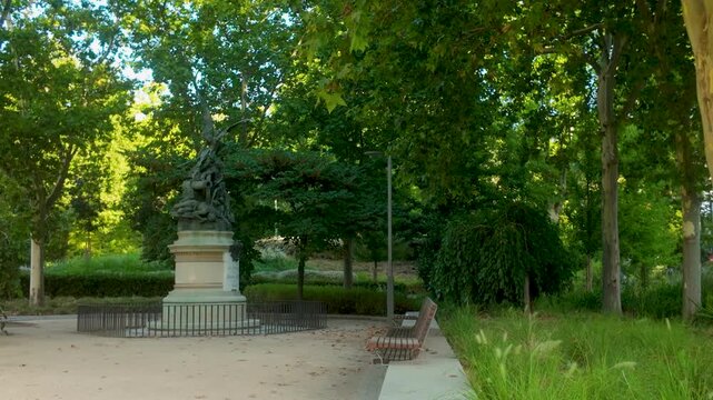A serene view of the famous Fallen Angel monument surrounded by lush green trees in Buen Retiro Park, Madrid, Spain. Captures urban nature and historical art.