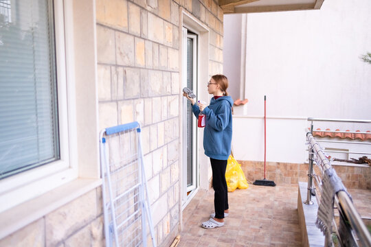 Teenage girl cleaning a balcony window with spray and cloth.
