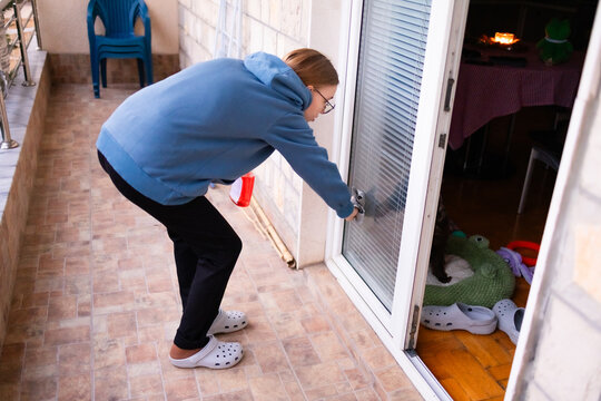Teenage girl cleaning a balcony door with spray bottle and cloth.