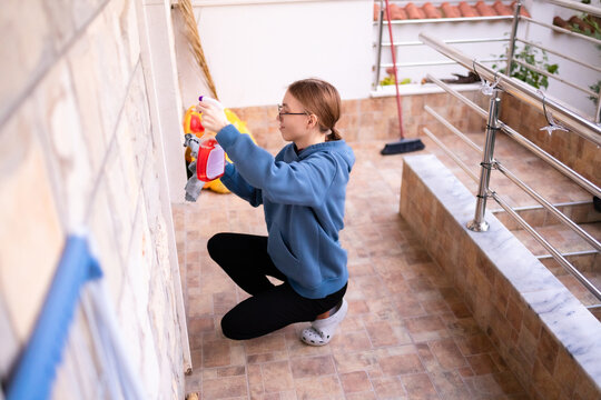 Teenage girl cleaning the lower frame of a balcony door.