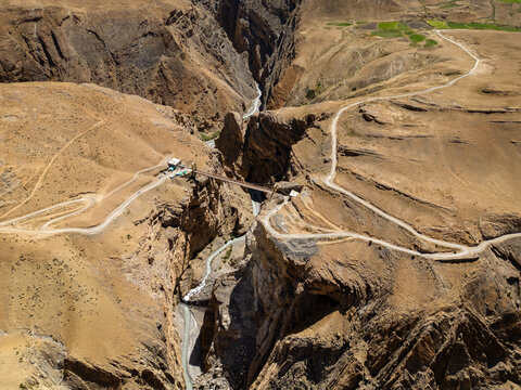Aerial view of Chicham Bridge spanning a deep gorge with winding dirt roads and arid mountain terrain in Chicham, Himachal Pradesh, India.