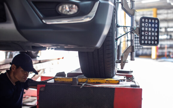 Selective focus to Mechanic checking car wheel alignment and suspension balancing with computerized sensor equipment in an auto service garage workshop. Bright background.