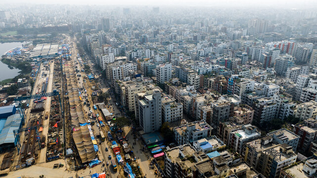 Aerial view of the dense urban landscape of Tongi with residential buildings, a construction site along the main road, and hazy sky in Tongi, Dhaka Division, Bangladesh.