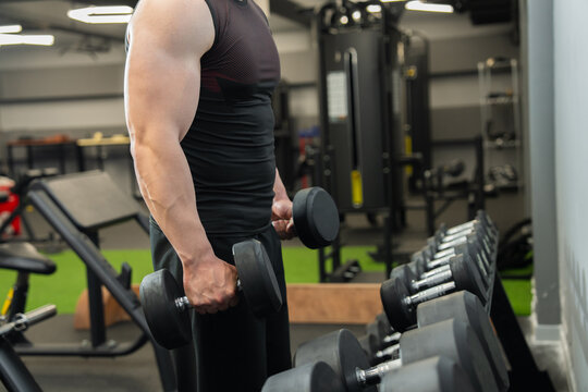 A muscular man trains with dumbbells. Brutal, strong, athletic men pump up their muscles. Concept: A bodybuilder performs exercises in the gym.