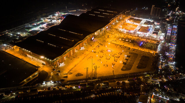 Aerial view of a bustling night fair with illuminated exhibition tents, crowds of people, and parked vehicles in Dhaka, Dhaka Division, Bangladesh.