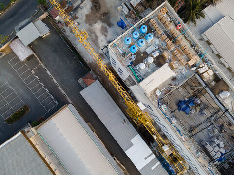Aerial view of a construction site featuring a yellow tower crane, a building with water tanks on the roof, and adjacent parking areas in Purwokerto, Central Java, Indonesia.
