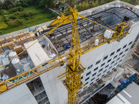 Aerial view of a large yellow tower crane positioned over a modern building under construction with visible scaffolding and surrounding greenery in Purwokerto, Central Java, Indonesia.