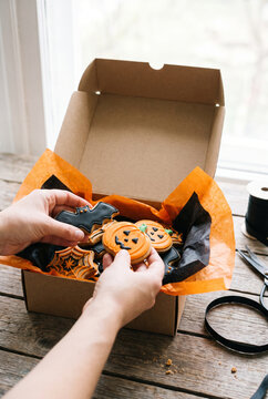 Person holding Halloween-themed cookies in a gift box  