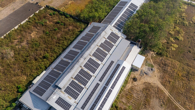 Aerial view of a large industrial building covered with solar panels, situated amidst rural fields and trees in Klaten, Central Java, Indonesia.