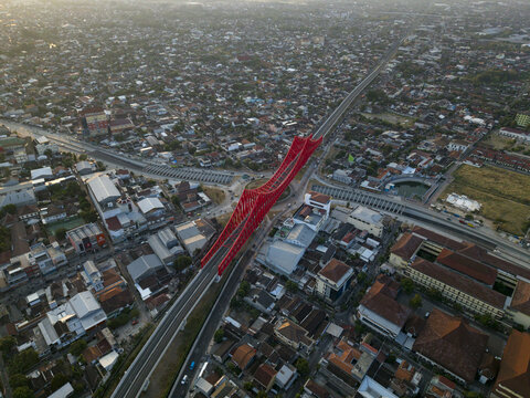 Aerial view of the red Joglo Railway Bridge spanning over the urban landscape of Kecamatan Banjarsari, Jawa Tengah, Indonesia.
