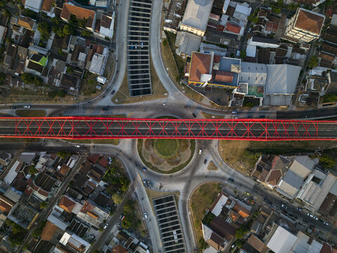Aerial view of Joglo Railway Bridge with its red steel truss structure spanning over a roundabout in Kecamatan Banjarsari, Jawa Tengah, Indonesia.