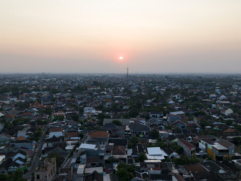 Aerial view of the dense residential rooftops of Kecamatan Banjarsari at sunset with a warm glow over the horizon in Kecamatan Banjarsari, Jawa Tengah, Indonesia.