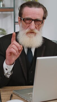 Senior old businessman working on laptop computer shakes finger and saying No be careful scolding and giving advice to avoid danger mistake disapproval sign at office. Confident freelancer elderly man