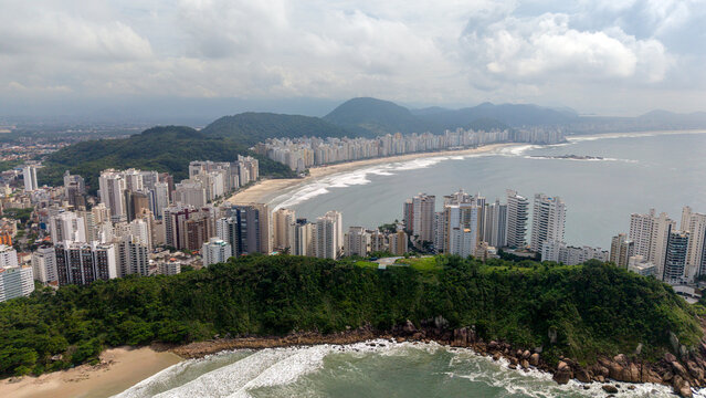 Aerial view of Pitangueiras Beach featuring high-rise buildings along the coastline, sandy shores, and lush green hills in the background in Guaruja, State of Sao Paulo, Brazil.