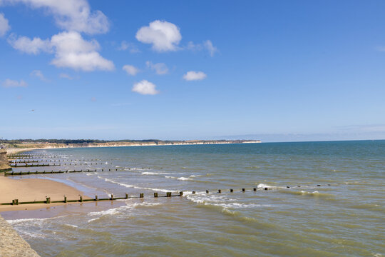 Coastal view from Bridlington across the sandy beach and North Sea with wooden groynes extending through shallow waves towards distant cliffs beneath a blue sky and clouds