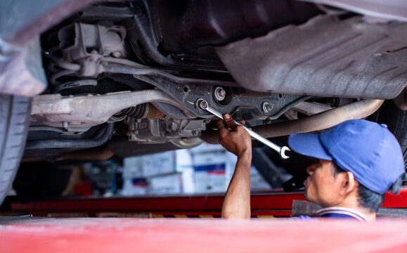 Selective focus to Professional mechanic using a wrench tool to repair and adjust the undercarriage suspension system of a car on a hydraulic lift in a garage workshop.