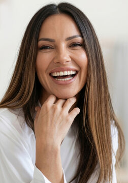 Portrait of a happily laughing woman with long dark hair holding hand under chin.