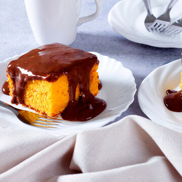 Slice of Brazilian carrot cake topped with creamy, glossy chocolate on a white plate, accompanied by a cloth napkin