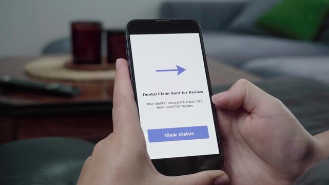 Close-up of hands using a mobile app that confirms a dental insurance claim has been sent for review with a view status button.