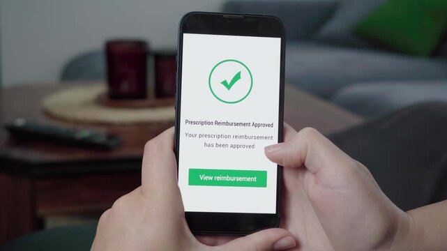Close-up of hands using a mobile health app that confirms a prescription reimbursement has been approved with a large check icon.