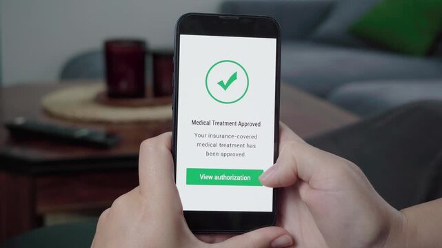 Person checks a health insurance app on a phone and taps a medical treatment approved authorization button.