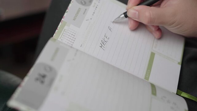 Female hand writes a doctor appointment reminder in a lined November day planner, noting personal health scheduling.
