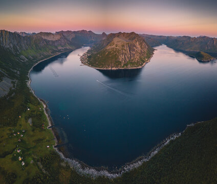 Aerial view of the scenic Gryllefjord surrounded by dramatic mountains and calm deep blue waters under a soft sunset sky in the Arctic region. Gryllefjord, Troms, Norway.