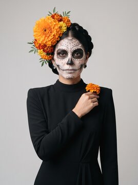 Persona con maquillaje de Catrina y flores de cempas&uacute;chil para el D&iacute;a de Muertos, retrato con vestido negro sobre fondo neutro