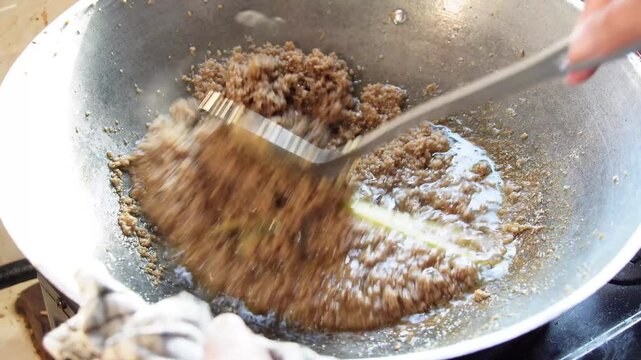 Close-up of minced meat sizzling in wok with lemongrass stalks being stirred. Authentic Asian cuisine preparation. High detail food cooking scene for culinary content.