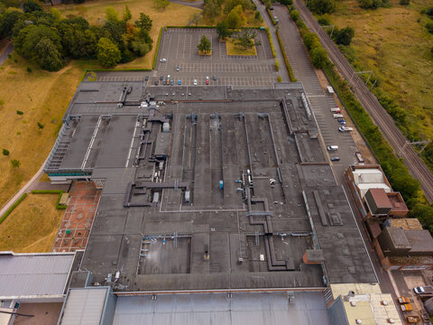 Barlaston, United Kingdom - 16 August 2026: Aerial view of the World of Wedgwood complex, featuring a large industrial building with a flat roof, HVAC systems, and adjacent parking lot.