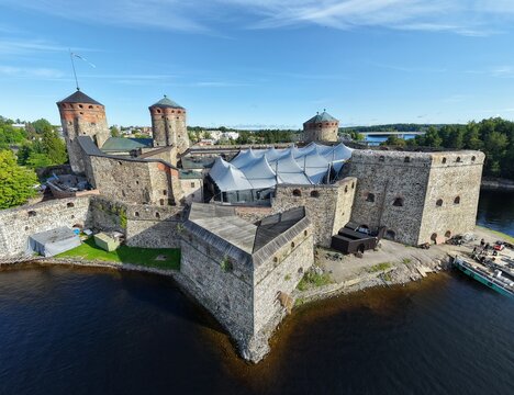 Aerial view of Olavinlinna, a medieval stone castle on an island with high towers, stone walls, and a white tent structure in the courtyard in Savonlinna, South Savo, Finland.