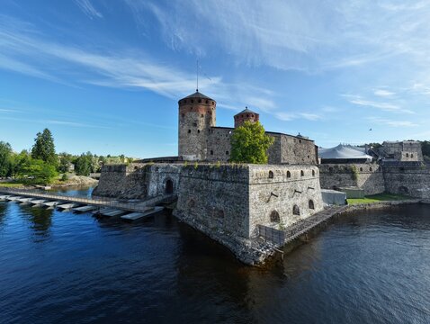 Aerial view of Olavinlinna castle surrounded by water, stone walls, and blue sky in Savonlinna, South Savo, Finland.