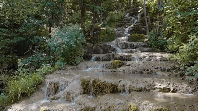 Scenic view of Bigar waterfall cascading over mossy tufa rock steps in a dense forest near Kalna, Stara Planina, Serbia. Cinematic pure nature stream footage shot in summer.